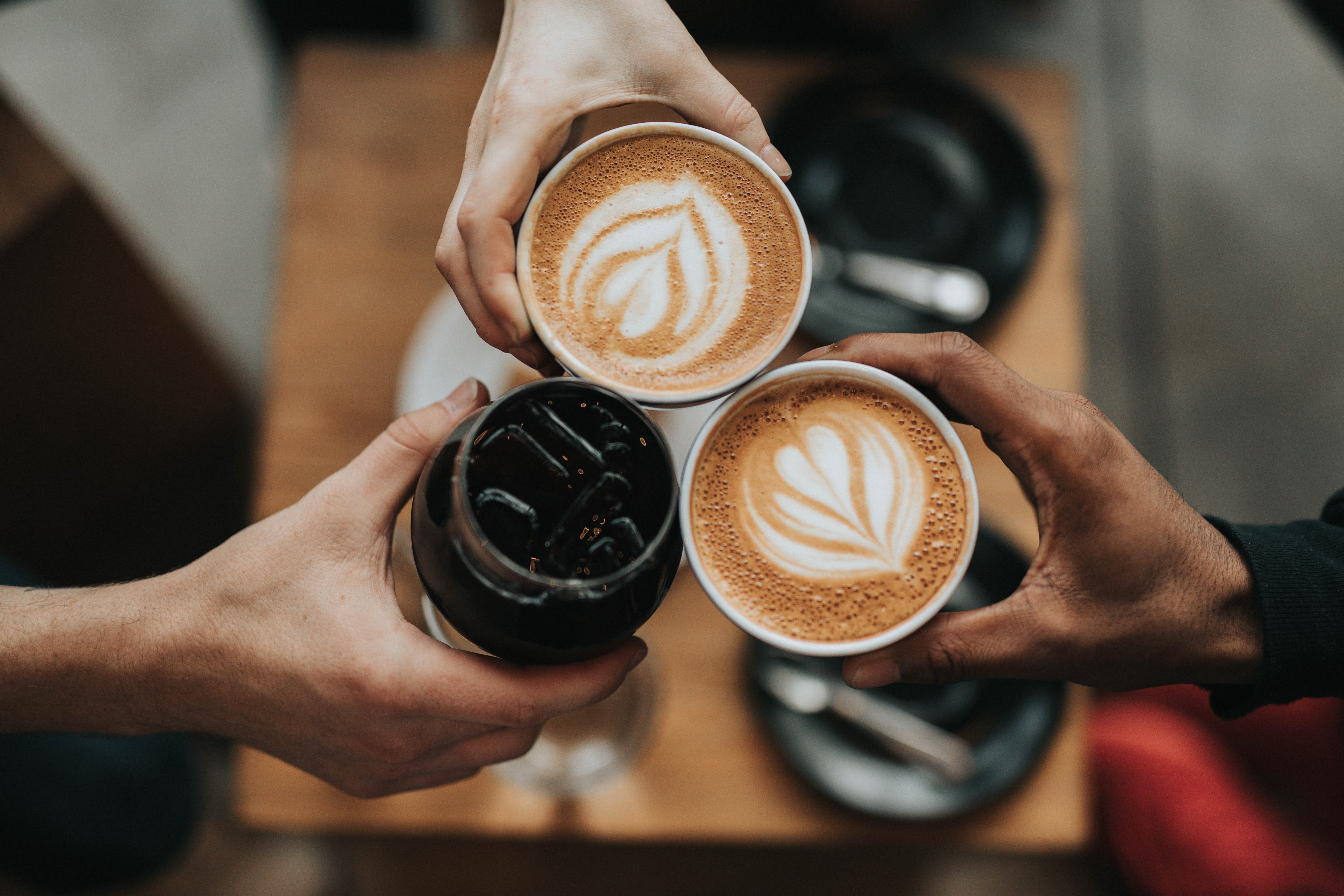 Three hands each holding a coffee in the center of the image.